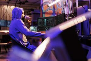 Hacker drinking coffee and doing illegal activities on computer late at night. Criminal holding beverage to go while cracking password and using malicious software in abandoned warehouse photo