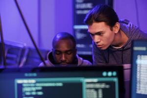 Hackers analyzing and discussing malicious code on computer screen, planning internet crime. Two criminals talking about scam scheme and doing illegal activity late at night photo