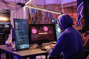 Criminal in hood successfully hacking into computer system in abandoned warehouse. Hacker gaining unauthorized access and stealing valuable data from database online server photo