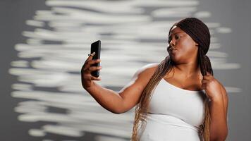 African american woman feeling confident taking photos, using smartphone to show self love and body positivity. Female model playing around in studio to promote self confidence, radiant skin. photo