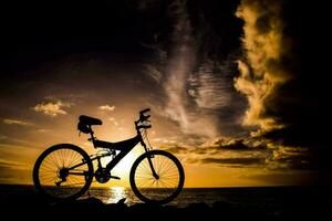 silueta de un bicicleta en el playa a puesta de sol foto