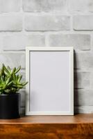 Empty vertical picture frame mockup hanging on a brick wall with wooden desk table and flower vase AI Generated photo