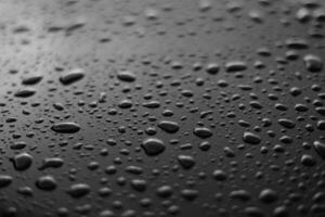 Rain or water drops different size on a black shiny car hood surface. Water droplets on dark iron surface and texture. Abstract background and water texture for design. photo