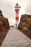 a red and white lighthouse stands in the middle of a rocky area photo