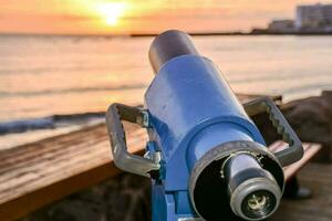 un telescopio en un banco con vista a el Oceano a puesta de sol foto