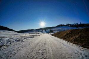 a dirt road in the snow with the sun shining photo