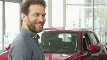 content mature homme souriant montrant le sien voiture clés à le concession salle d'exposition video