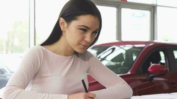 Beautiful young woman signing papers at the dealership showroom video