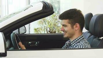 Happy young handsome man sitting in a new convertible at the dealership video