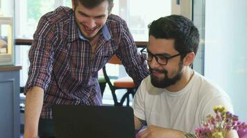 dois jovem homens usando computador portátil juntos às a café fazer compras video