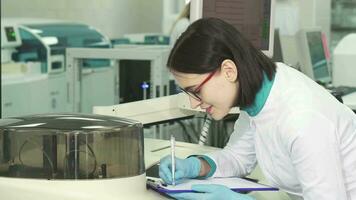 ung kvinna kemist tar anteckningar på de modern laboratorium video