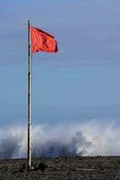un rojo bandera en el playa con olas estrellarse en el antecedentes foto