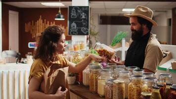 cliente falando com vendedor dentro orgânico Comida comprar, inquirindo sobre produtos ético abastecimento e Perguntando para recomendações. mulher dentro baixo carbono pegada loja conversando com comerciante sobre despensa grampos video