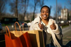 Outdoor portrait of happy black woman. She is sitting on bench in the street after shopping. photo