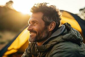 Portrait of man looking at camera while near camping tent at sunset AI generated photo