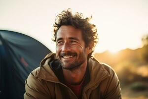 Portrait of man looking at camera while near camping tent at sunset AI generated photo
