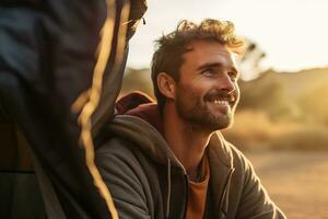 Portrait of man looking at camera while near camping tent at sunset AI generated photo