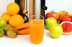 un vaso de recién exprimido Fruta jugo, Fruta y un moderno exprimidor en el mesa en el cocina. hecho en casa sano Fruta y vegetal jugos selectivo enfocar. de cerca. foto