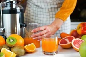 A young woman prepares healthy juice from a variety of ripe fruits in the kitchen at home. Close-up. Selective focus. photo