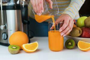 hembra manos verter recién exprimido Fruta jugo dentro un vaso. natural y sano jugos de cerca. foto