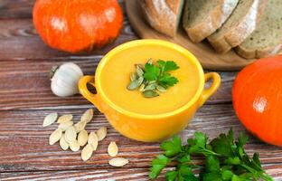 Pumpkin cream soup and freshly baked homemade bread on a wooden background. Close-up. photo