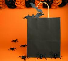 Halloween shopping and sale concept. Paper black bag and decor for Halloween on orange background. Mock up. Copy space. Selective focus. photo