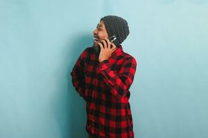 contento joven asiático hombre es riendo escuchando gracioso chistes en su teléfono llamar, aislado en azul antecedentes foto