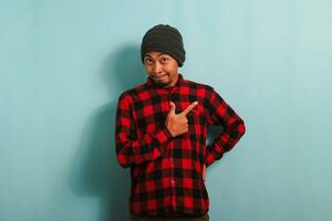 Excited Young Asian man is pointing his finger right at the copy space, isolated on blue background photo