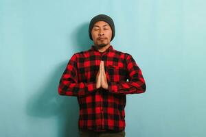 Calm young Asian man is meditating and practicing yoga while standing against a blue background photo