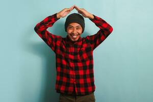 Happy young Asian man making roof gesture above his head, isolated on blue background photo