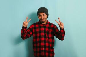 Attractive young Asian man poses for the camera and shows peace gesture, isolated on blue background photo