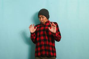 Ew, It's so gross. An annoyed young Asian man with a beanie hat and a red plaid flannel shirt is repulsed by something, displaying a disgusted expression while standing against a blue background photo