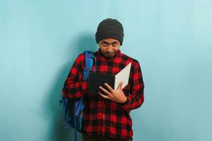 Pensive young Asian student is deep in thought, looking ideas while standing against blue background photo