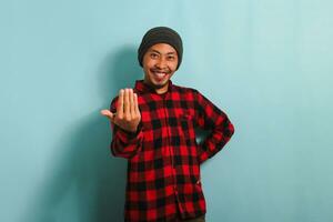 A young Asian man is making a Come Here gesture, inviting, welcoming, isolated on blue background photo