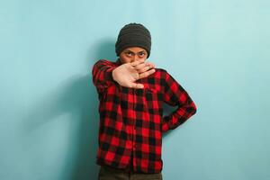 Angry young Asian man stands with his arms crossed, stop gesture, isolated on blue background. photo