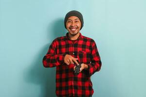 Happy young Asian man holding a TV remote while watching a movie, isolated on a blue background photo