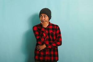 Thoughtful Young Asian man holds his chin, making plans, isolated on a blue background photo