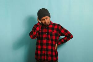 Young Asian man holds his hand near his ear, suffering from earache, isolated on blue background photo