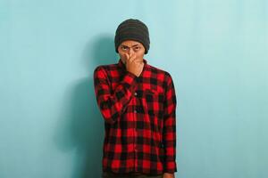 Annoyed young Asian man holds his breath smells something stinky, isolated on blue backdrop photo