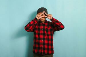 Young Asian man with beanie hat and red plaid flannel shirt making a triangle gesture with palms, symbolizing the environment protection, recycling, and reusing concept, isolated on a blue background photo