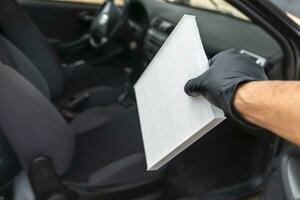 A black gloved hand holding a car pollen filter. Vehicle maintenance concept. photo