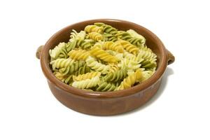 Spiral pasta of three colors, served in a clay bowl. Isolated on a white background. Vegetarian food concept. photo