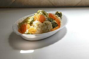 Plate of cooked vegetables, cabbage, broccoli, carrots and potatoes. A ray of light on the plate. Healthy food concept. photo