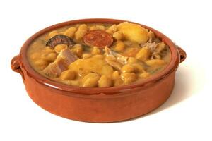 A chickpea soup in a clay bowl, isolated on a white background. This comforting chickpea stew combines traditional flavors such as chorizo, black pudding and vegetables, creating a aromatic dish. photo