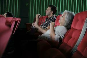 Various people enjoy watching cinema in movie theaters. Senior Asian woman and male audience have a fun indoor entertainment lifestyle with film art shows, happy and cheerful with popcorn and a smile. photo