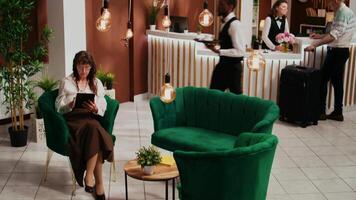 Hotel cliente utilizzando moderno aggeggio nel ricezione, in attesa per dai un'occhiata nel e navigazione punti di riferimento su in linea pagina web. anziano persona su vacanza utilizzando Internet dopo in arrivo a cinque stella ricorrere. video