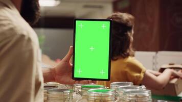 Customer uses mockup tablet in zero waste supermarket to check ingredients for healthy recipe, close up. Client in eco bio local shop with green screen device while shopping for pantry staples video