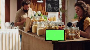 Customers shop next to chroma key tablet with copy space used as commercial sign in zero waste shop. Promotional ad on green screen device in food store with products in reusable decomposable package video