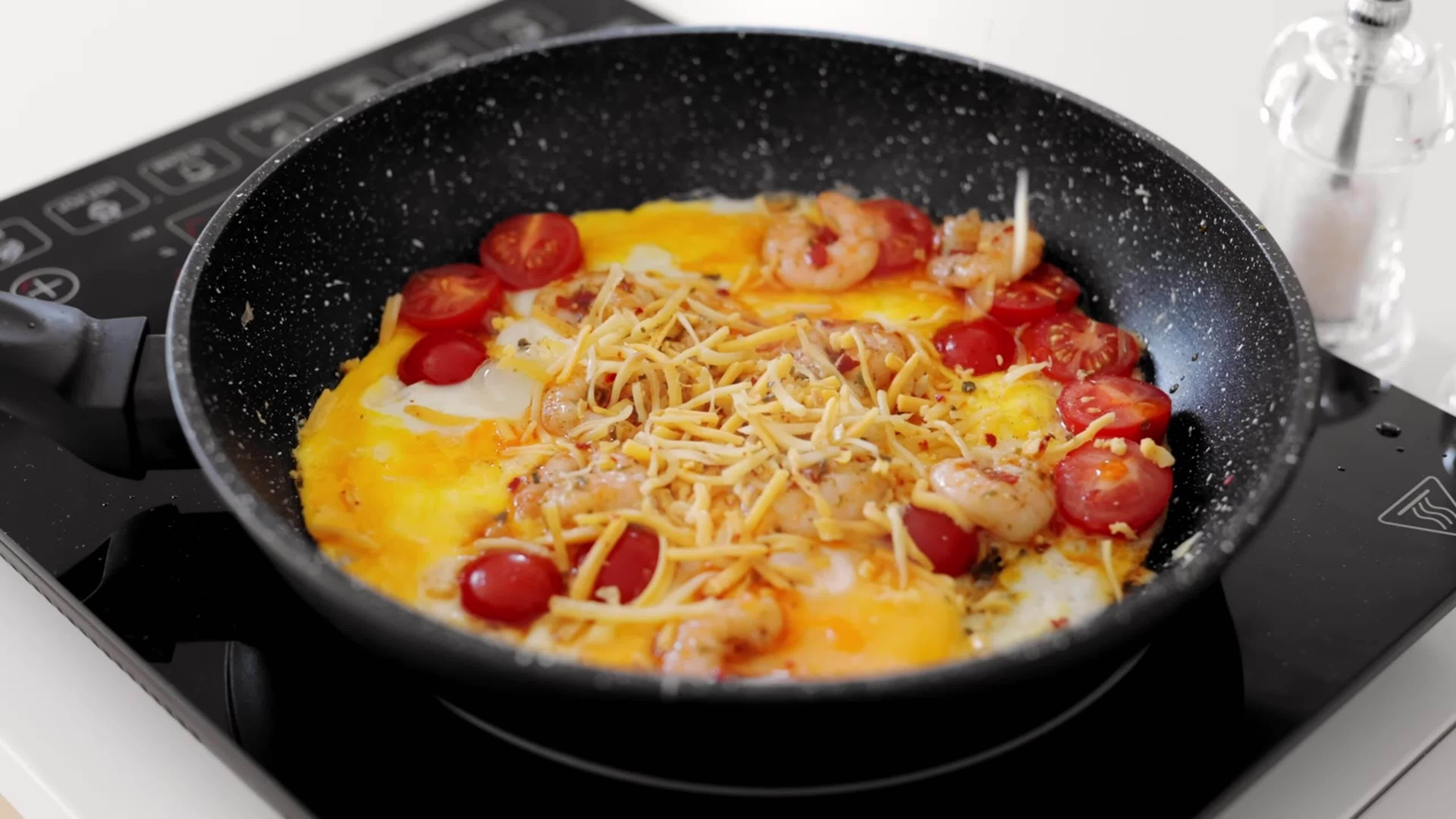 Omelette with cherry tomatoes, vegetables and shrimps in a pan at home