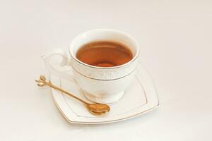 blanco taza con platillo y dorado cuchara y té hojas foto